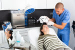 A dermatologist carefully placing the Light Therapy Face Mask on a patient's face, ensuring proper fit for effective treatment. The mask is designed for skincare and mood enhancement using LED light therapy.